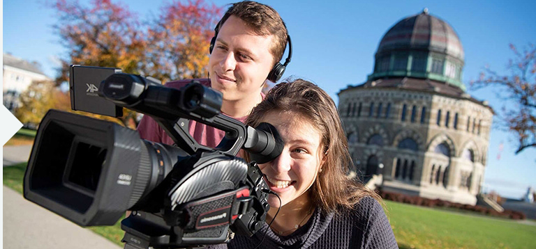 背景是诺特纪念馆，两名学生正在操作摄像机